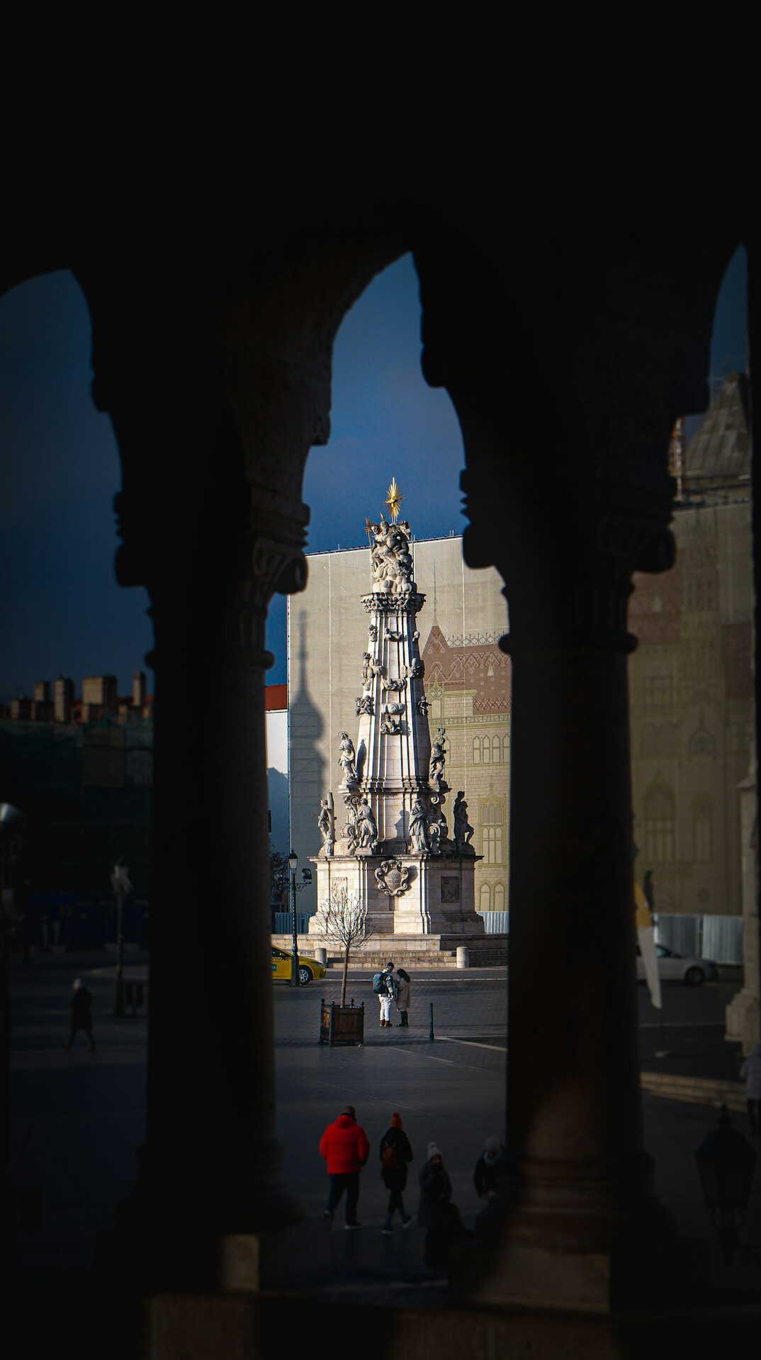 Distant anonymous silhouettes crossing a quiet European plaza at dusk